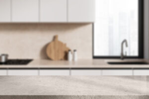 White stone product display table located in stylish blurry kitchen with beige walls, white cabinets and window. 3d rendering