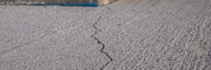 A visible crack runs through the surface of a concrete pavement near the corner of a building.