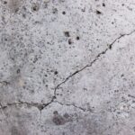 Cracked concrete surface with visible small holes and rough texture.
