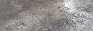 Wet, textured concrete patio surface with a dark, mottled finish next to a light-colored wall.