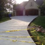 Freshly poured concrete driveway in front of a house, blocked off with caution tape to prevent entry.