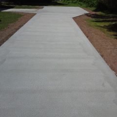 A newly poured concrete sidewalk leads to a house, bordered by grass and soil on both sides.