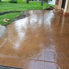 A newly poured, stamped concrete patio with a wet, glossy finish in a suburban backyard.