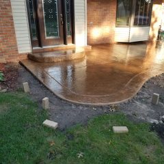 Freshly poured and finished concrete porch and walkway in front of a brick house, with landscape edging in place.