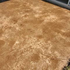 Textured brown concrete patio near a sliding glass door with some grass visible at the edge.
