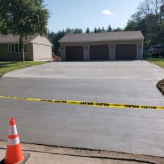 Freshly poured concrete driveway in front of a triple garage, blocked off with caution tape and a traffic cone.