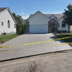 Fresh concrete driveway in front of a house, blocked off with yellow caution tape, on a sunny day.