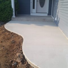 Freshly poured concrete porch with a curved edge in front of a blue house with a white door and pillar.
