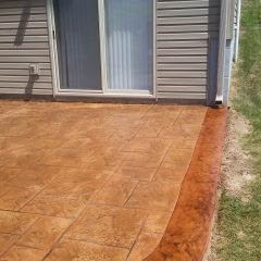 Stamped concrete patio with a brown border adjacent to a house with beige siding and sliding glass doors.