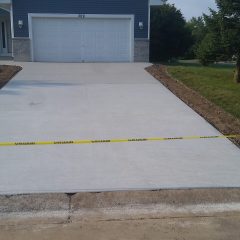 Freshly poured concrete driveway in front of a blue house, blocked off with yellow caution tape.