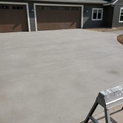 Freshly poured concrete driveway in front of a three-car garage attached to a modern house. A step ladder is in the foreground.