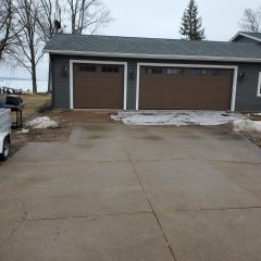 Concrete driveway leads to a two-car garage with brown doors; patches of melting snow are visible on the ground.