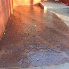 A driveway with a stamped and stained concrete surface in front of a red exterior wall and steps.