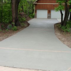 Freshly poured concrete driveway leading to a two-car garage with trees and greenery on both sides.