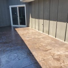 A concrete patio with a shadow dividing light and dark areas, next to a dark-paneled wall and sliding glass door.