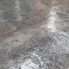Wet, textured concrete surface with visible patterns, next to a beige wall and some exposed soil at the edge.