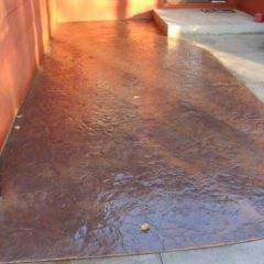 Brown stamped concrete patio with a textured surface adjacent to a house and concrete steps.
