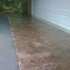 A stamped and stained concrete driveway in front of a white garage door and brick wall on a cloudy day.
