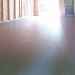 Freshly poured concrete floor inside a building under construction, with exposed wooden framing and windows.