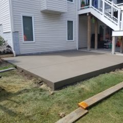 Freshly poured and leveled concrete patio slab behind a house with beige siding and white trim.